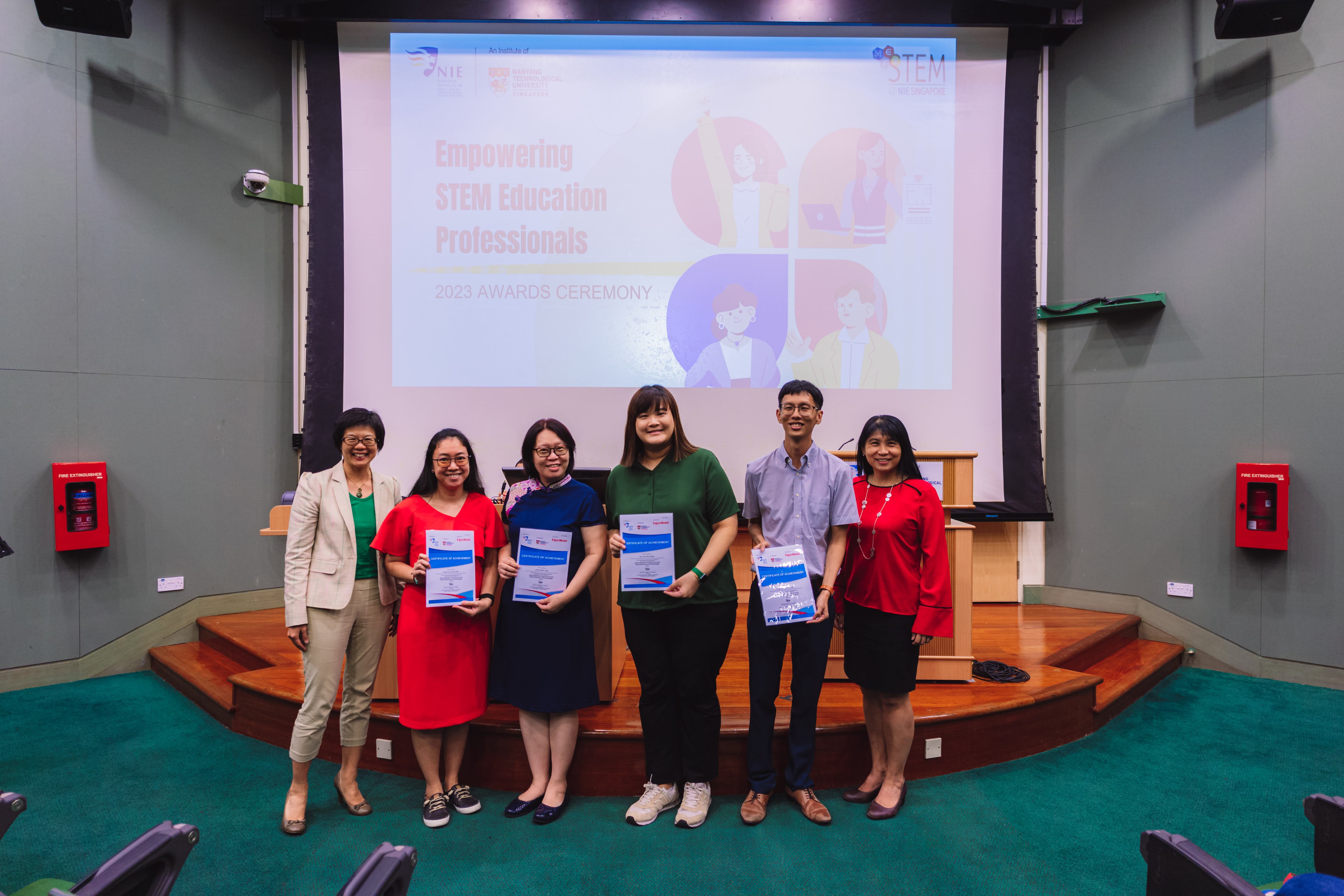 Six people stand before a projected slide reading Empowering STEM Education Professionals 2023 Awards Ceremony, holding certificates.